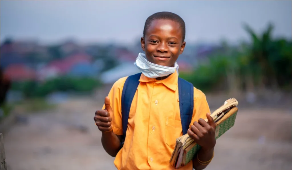 african boy, with face mask lowered at the chin, books in the hand