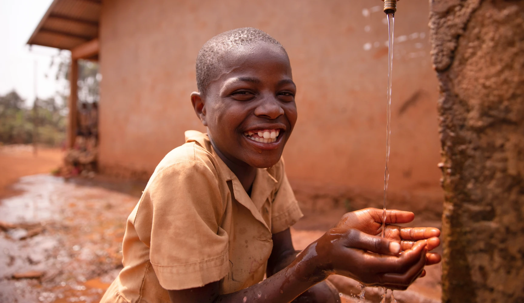 Smiling black african schoolboy drinking from a tap outside during recreation